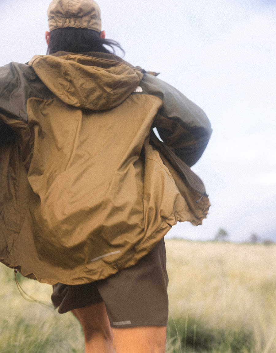 A person wearing khaki shorts, a yellow shirt, brown jacket and brown hat running