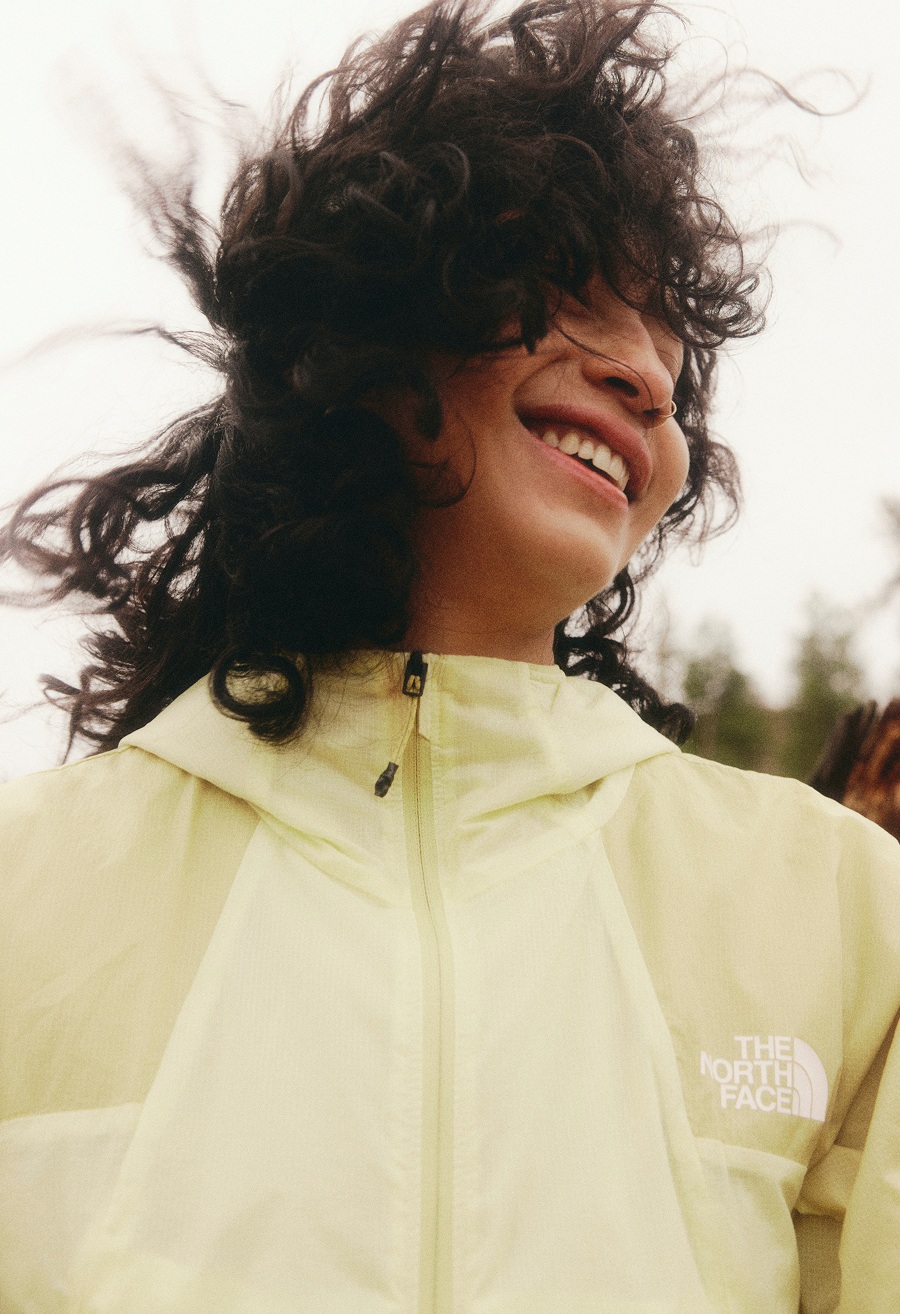 Une personne portant une veste jaune, avec des cheveux foncés et bouclés.