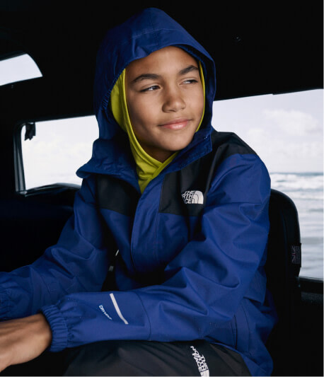 A boy looking out the window wearing a blue jacket with his hood up