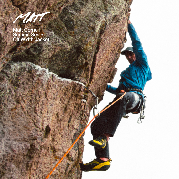 Person in blue jacket and black pants is climbing up a rock wall. 