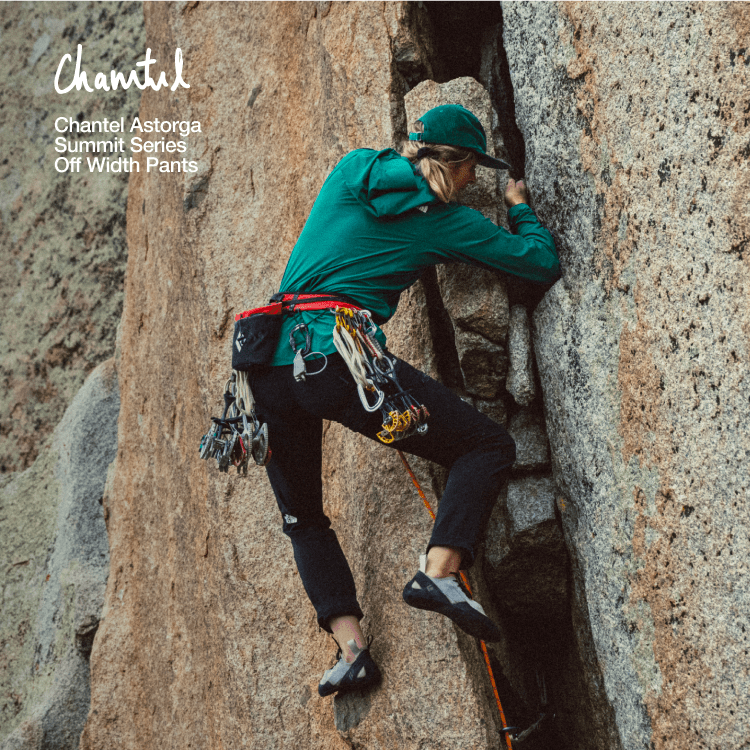Person in teal jacket and grey pants is climbing up a rock wall. 