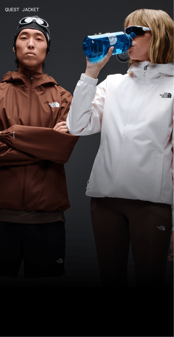Man standing with his arms crossed wearing a brown Quest Jacket and a woman drinking from a water bottle wearing a white Quest jacket.