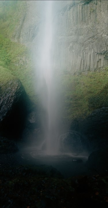 Rock wall covered in moss with a waterfall in the middle.