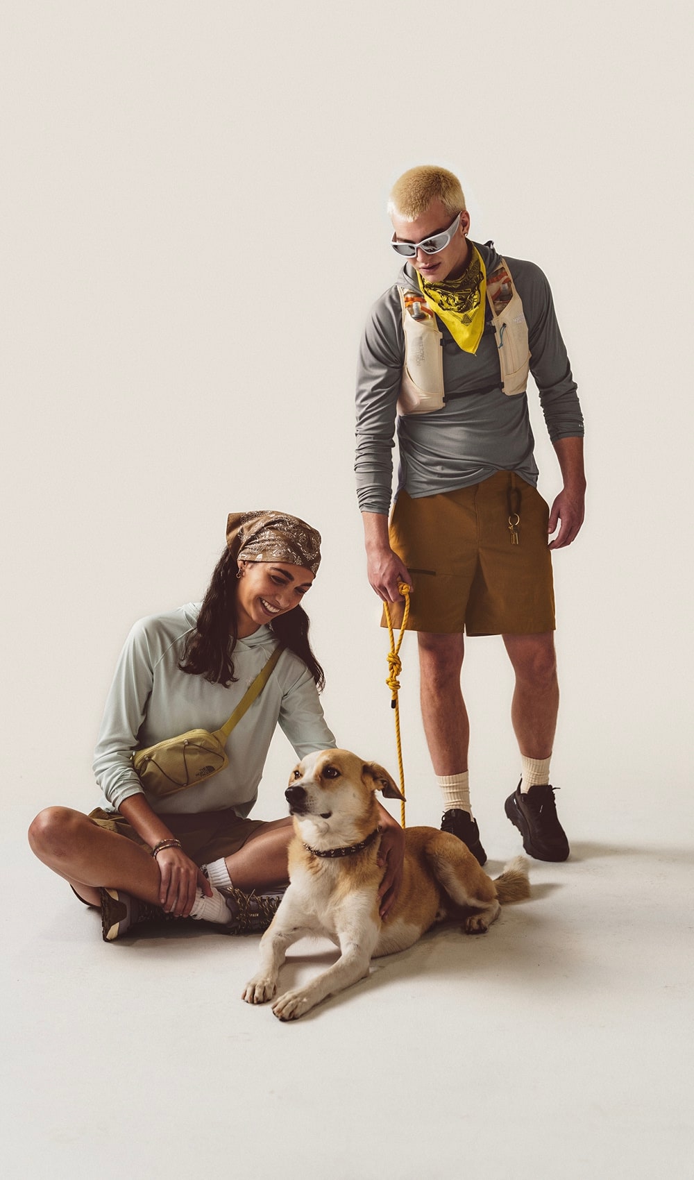Man standing wearing a long sleeve shirt and brown shorts looking down at a woman sitting petting a dog