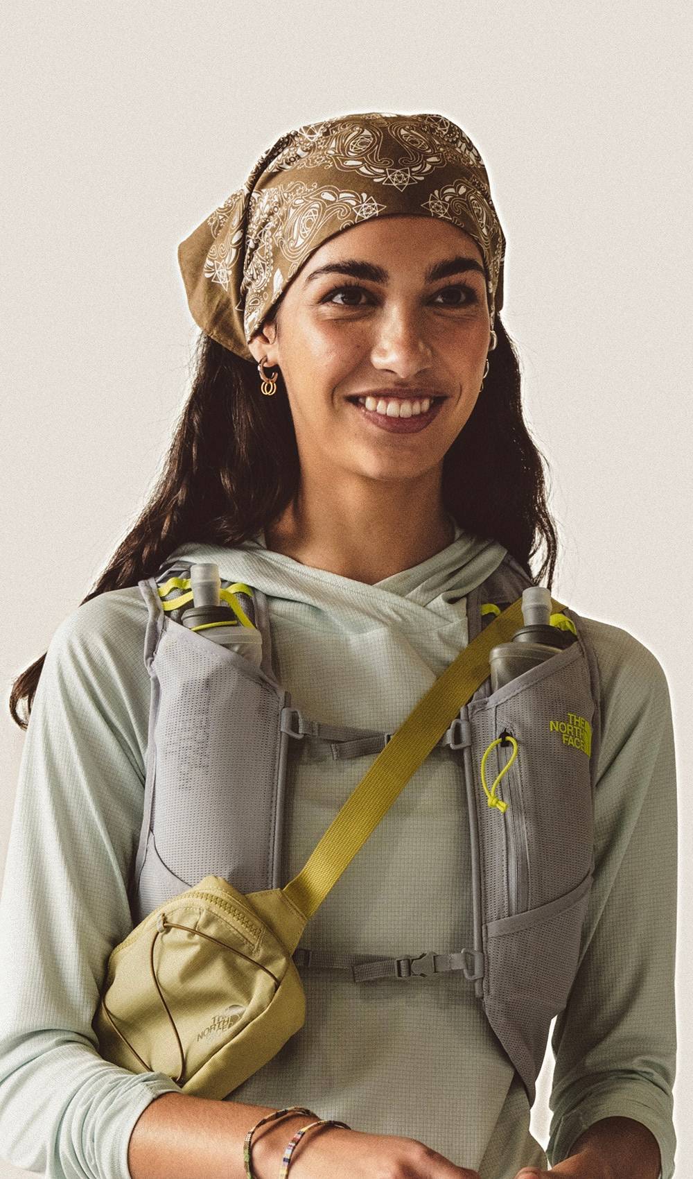 A woman smiling wearing a opal frost long sleeve hoodie and a grey running vest