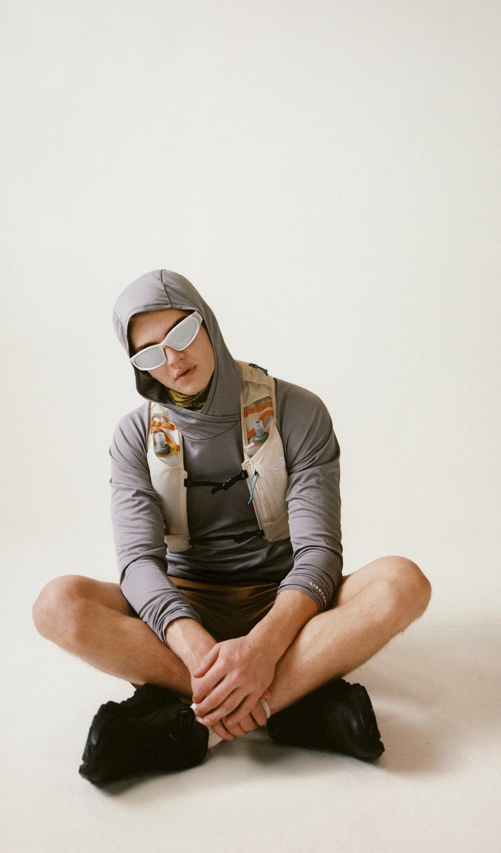 A man sitting criss cross wearing a grey long sleeve hooded shirt