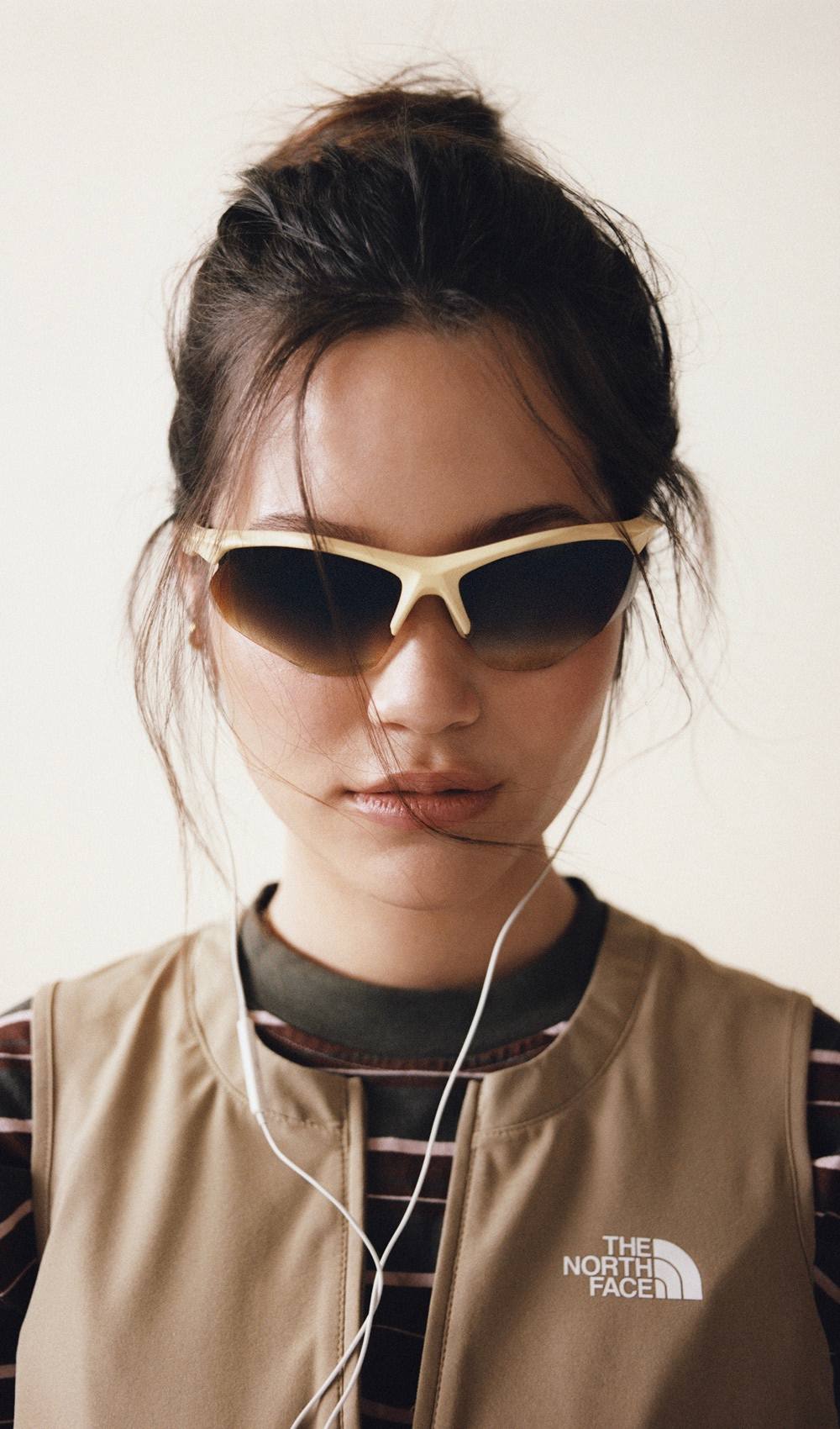 Closeup of a woman wearing sunglasses and wearing a striped shirt underneath a brown dress
