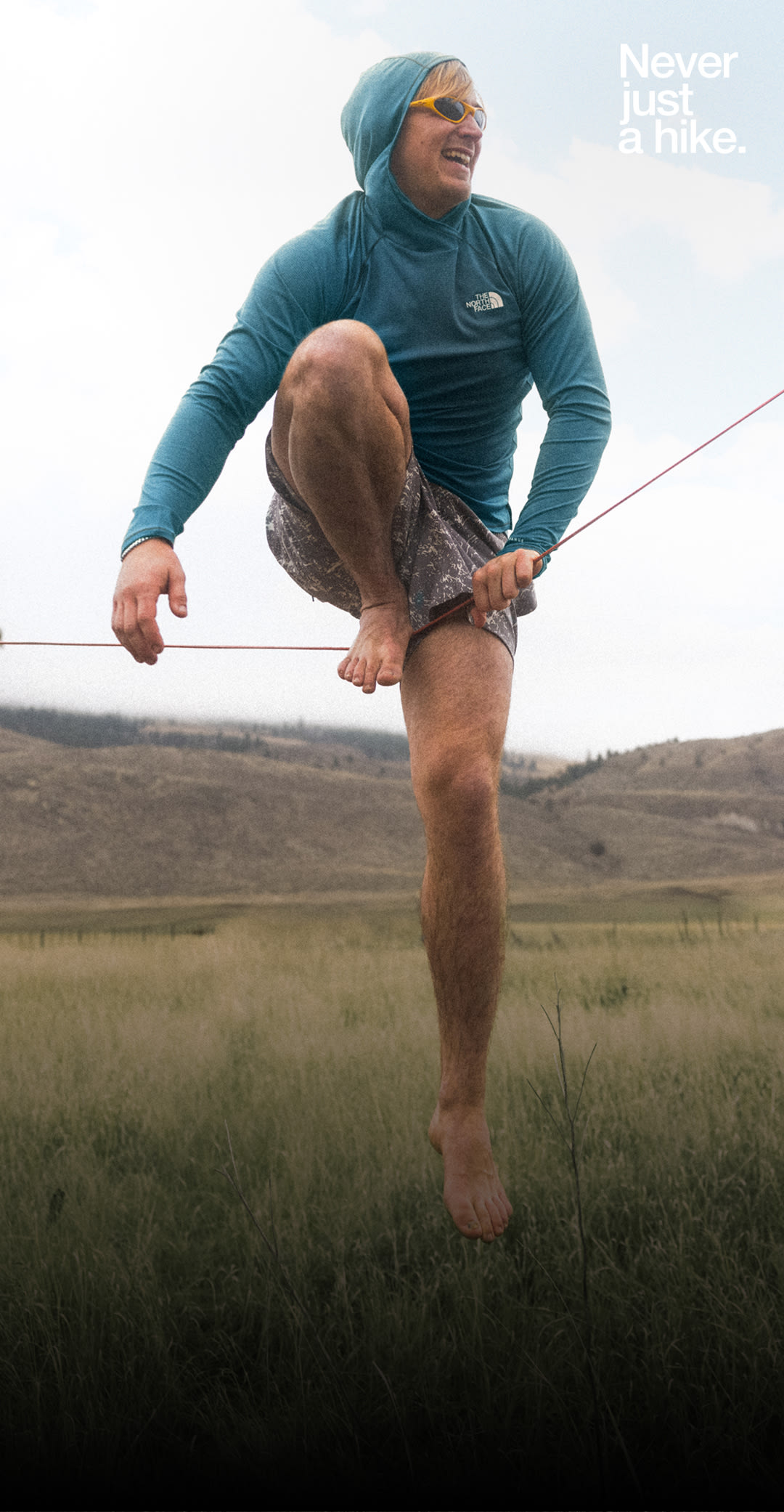 A person in a blue hoodie and shorts is having fun mounting a slackline. 