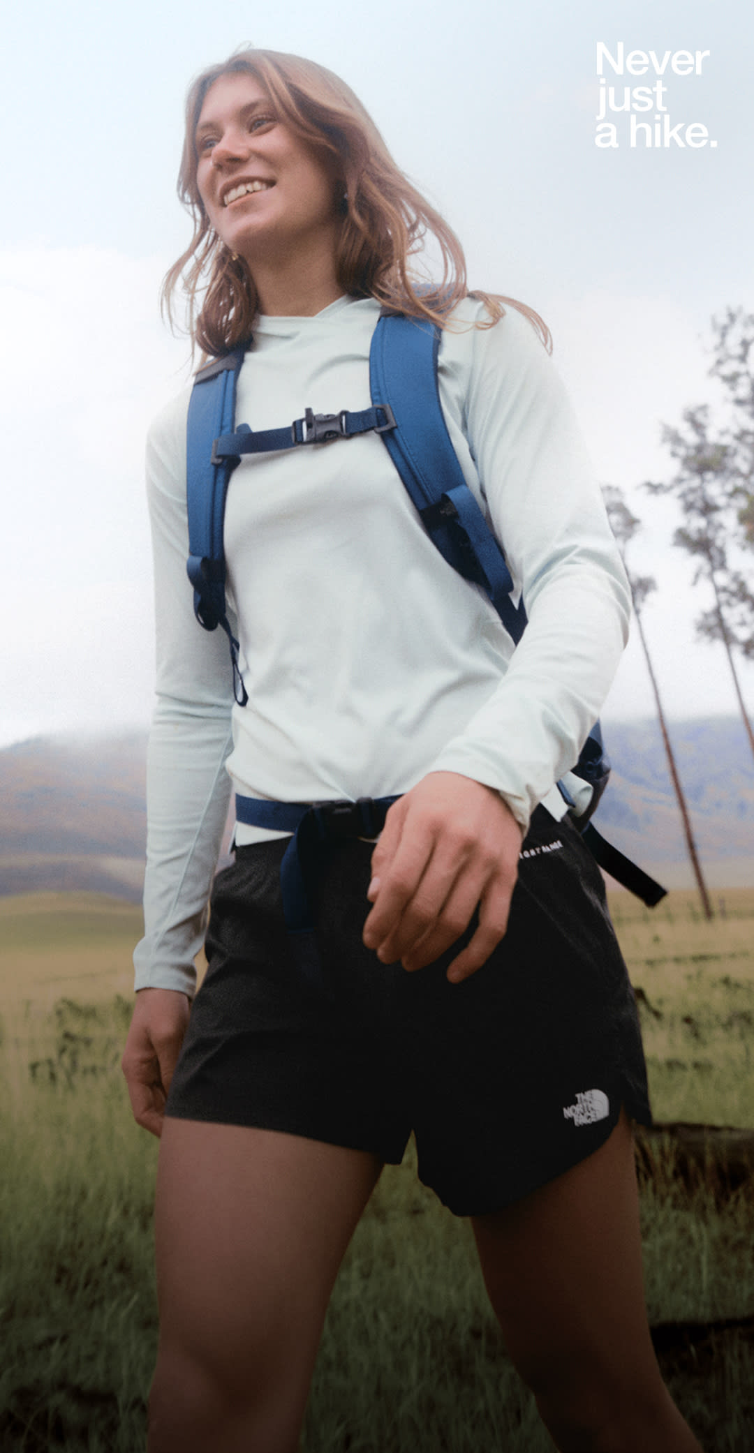 A person in a blue shirt with a blue backpack on is walking in a flat setting with hills in the background.