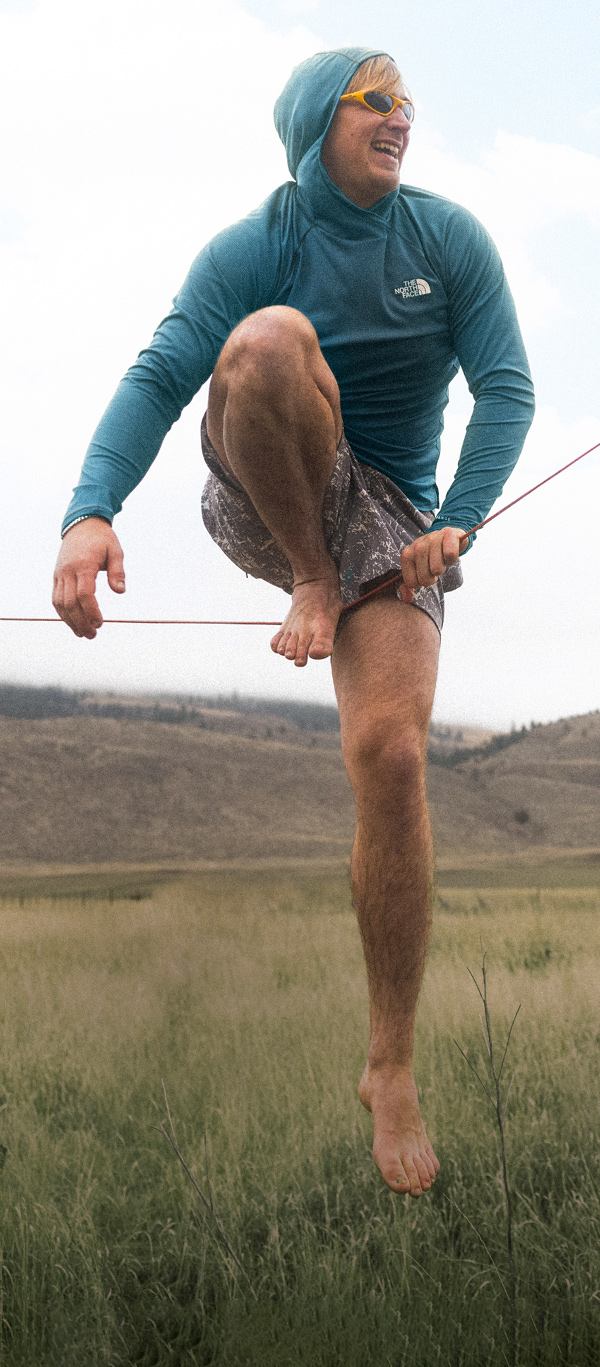 A person in a blue hoodie and shorts is having fun mounting a slackline.