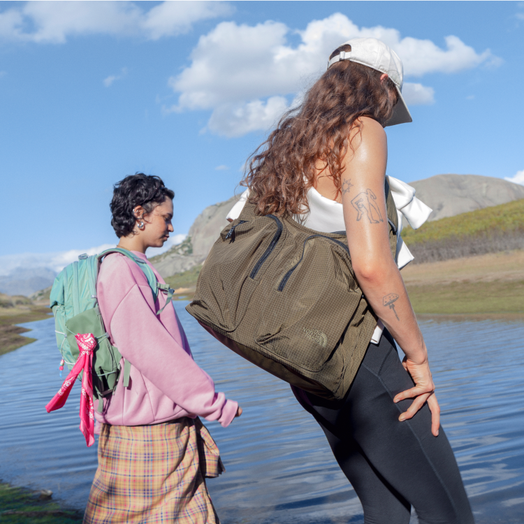 Two young people wearing packs walking along a small river.