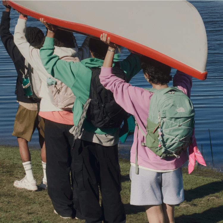 Quatre jeunes portant un sac à dos transportent ensemble un canot renversé.