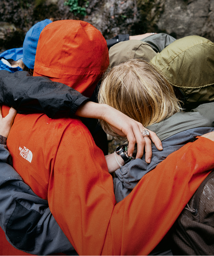 Group of young people wearing raingear huddling together in the rain.