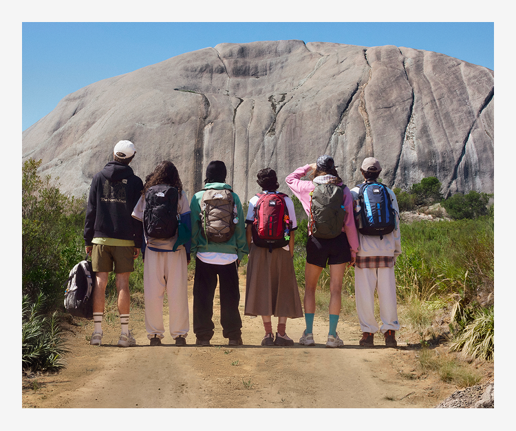 Five young people with their backs to the camera looking at a mountain in the distance. They are all wearing backpacks.