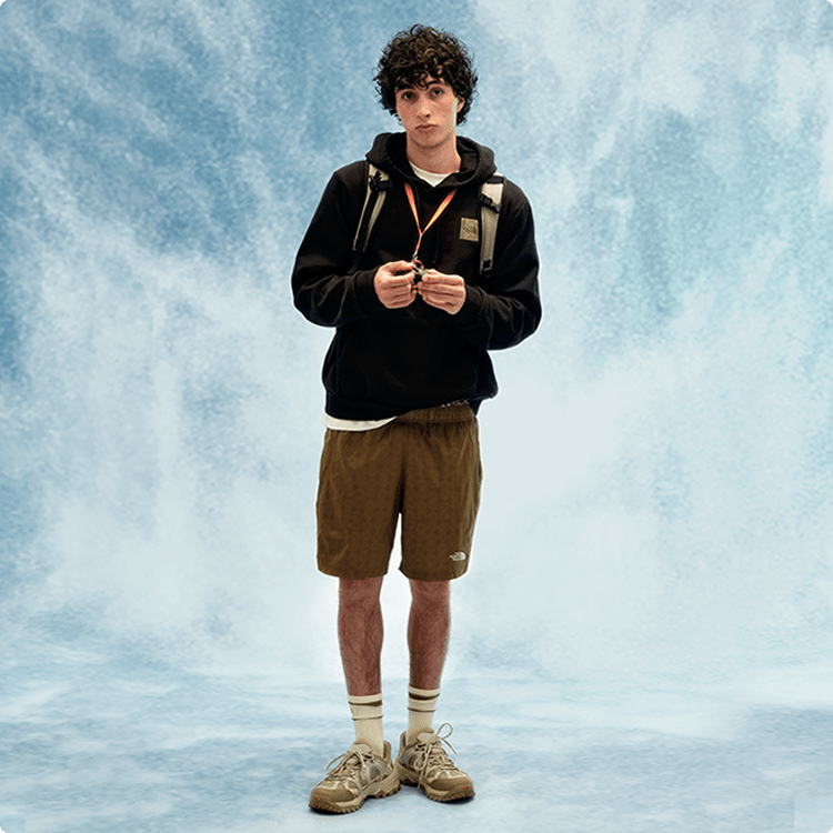 Jeune personne portant un chandail à capuchon noir et un short beige.