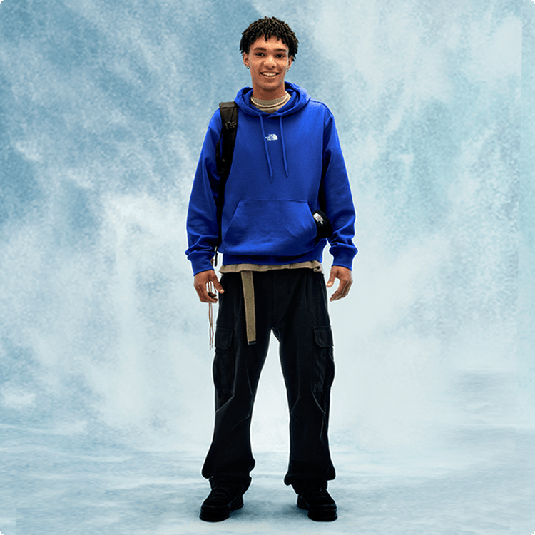 Un jeune homme portant un chandail à capuchon bleu, capuchon relevé et cordons serrés.