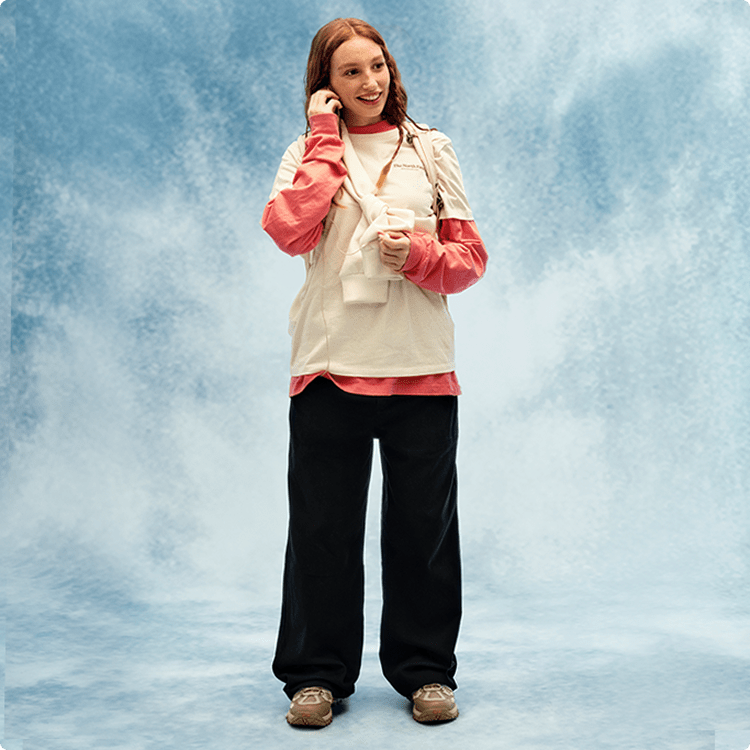 Une jeune femme portant un t-shirt blanc et un chandail à manches longues orange sourit.