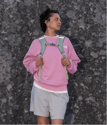 A girl wearing a pink oversized crew holding her backpack straps.