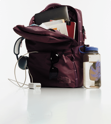 The Base Camp Voyager Daypack is fully in the frame, showing how many things can fit inside of it, plus a large water bottle to the side showing how big the water bottle holder is.