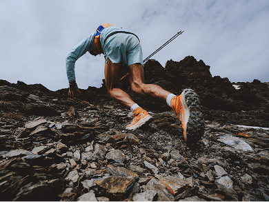Person wearing orange shoes is running up a rocky slope. Only the person’s legs are shown in the frame.