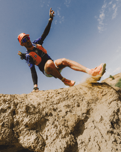 Person wearing an orange hat and orange vest is running down a dry, dusty slope.