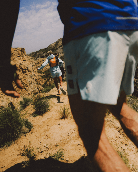 Two people wearing blue shorts and blue tops are running on high desert terrain.