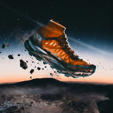 An orange Offtrail Ultra shoe is suspended in mid-air above a mountain, rocks are flying off of it, sunset in the background