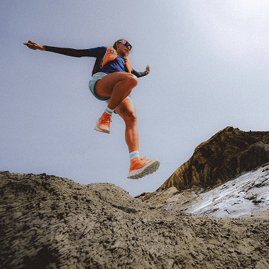 A person is bounding down a rock slope, wearing an orange Summit Series™ Run Vest.