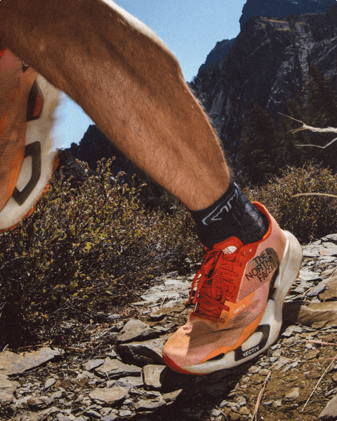 Close up of a red north face Vectiv shoe running up a trail.