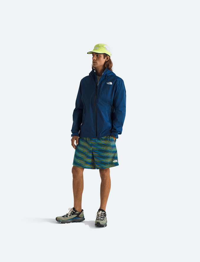 Un homme porte une veste de pluie bleue et un short.