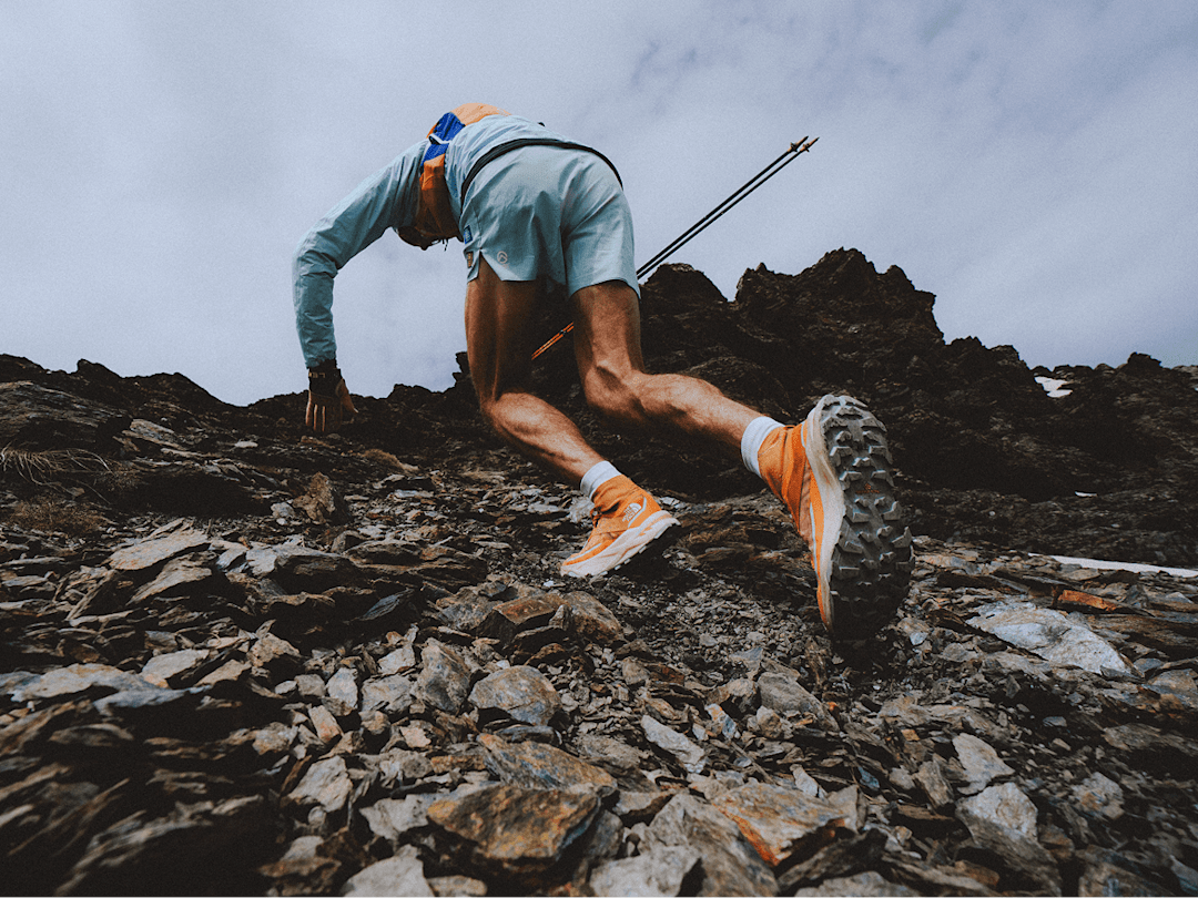 Person wearing orange shoes is running up a rocky slope. Only the person’s legs are shown in the frame.