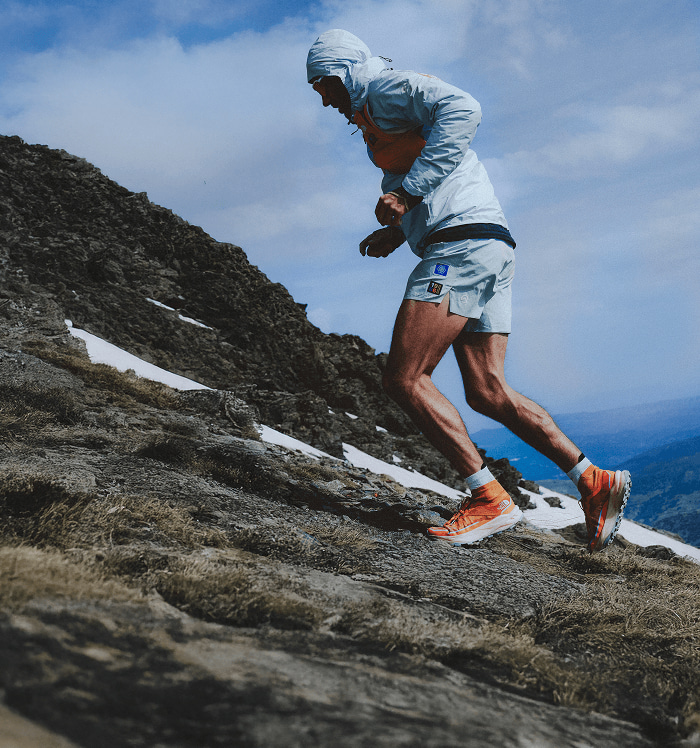 Une personne portant des chaussures orange et un short bleu gravit un terrain montagneux et rocheux.
