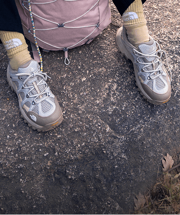 This image shows the bottom of a person’s legs wearing yellow socks and gray shoes, sitting on top of a rock.
