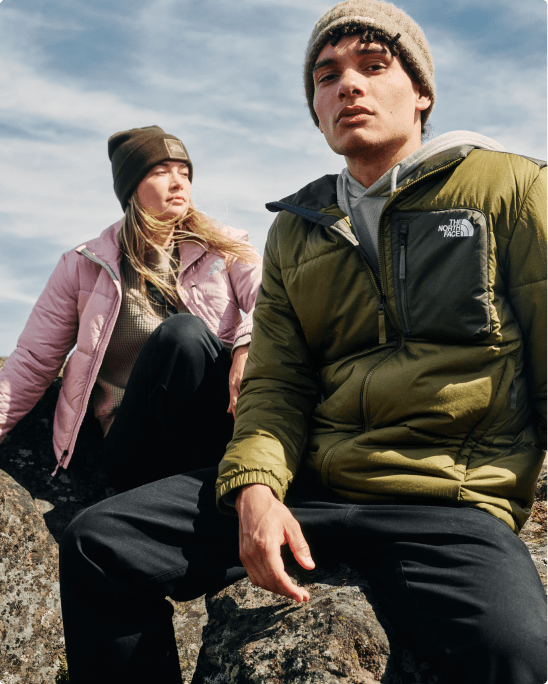 A man and woman sitting on a rock wearing Nuketo jackets