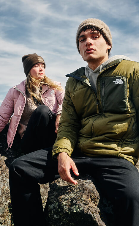 Two people wearing jackets and beanies walking across a mountainous landscape.
