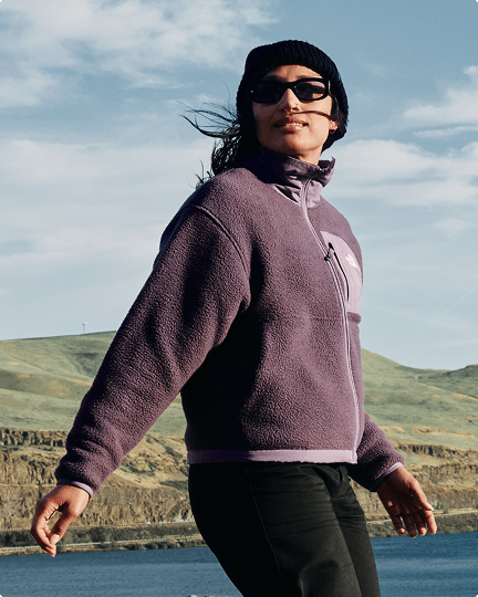 A woman walking along the coast wearing a purple Yumiori fleece