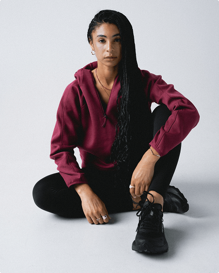 A woman sitting down wearing the Jaida hoodie on a grey background