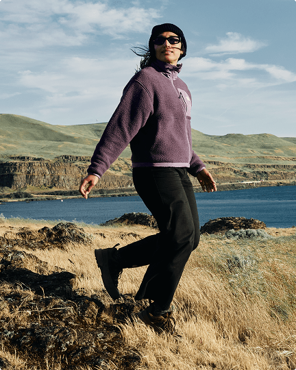 A woman walking along the coast wearing a purple full zip Yumiori
