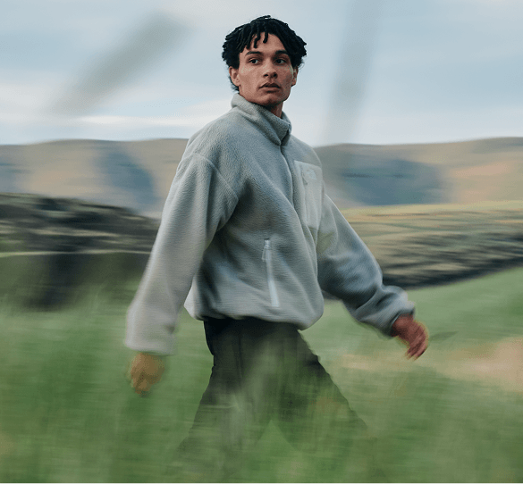 A man walking in the grass wearing a grey reversible Yumiori fleece