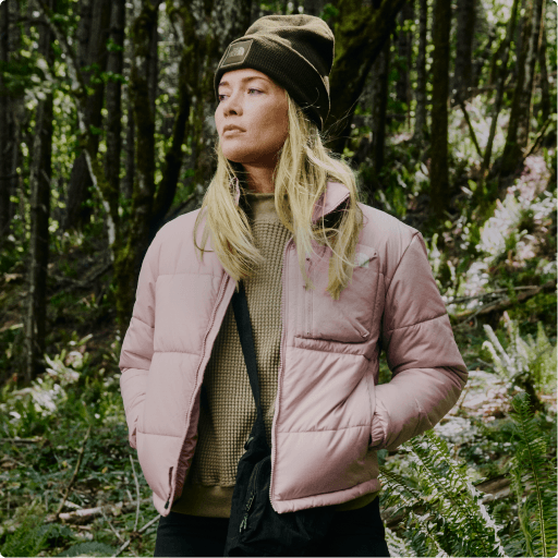 A woman wearing a pink jacket in the woods.