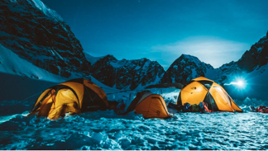 A snowy mountain campsite at dusk- multiple The North Face tents in Summit Gold.