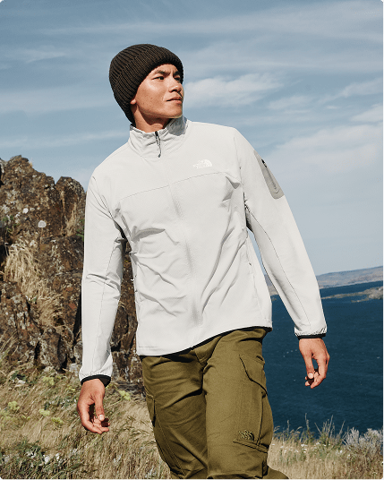 A person wearing a white jacket is walking outside on a grassy slope.