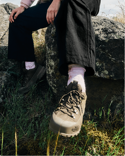 Closeup of a person’s shoe. They’re sitting outside on a rock, wearing black pants.