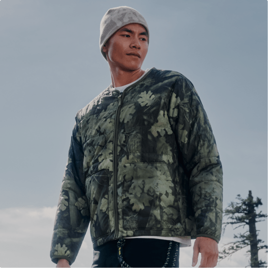 Une personne portant une veste à motif se tient à l’extérieur et regarde vers la gauche.