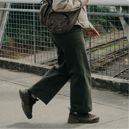 A person wearing green pants is walking on an overpass. 