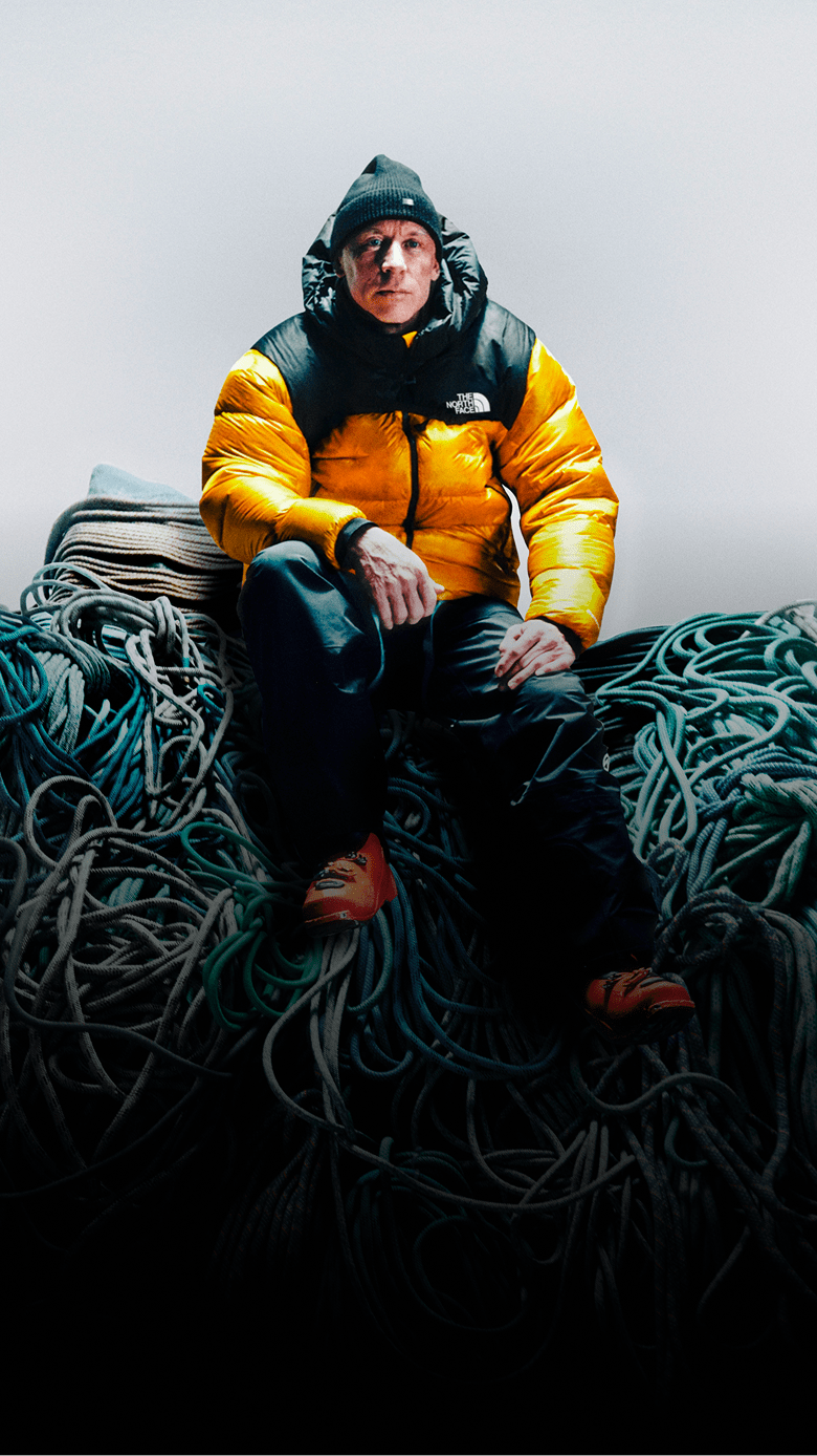 Jim Morrison is wearing a yellow Summit Nuptse jacket sitting on top of a pile of climbing rope.