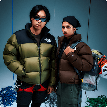 Two people standing in a studio wearing light brown and dark brown Retro Nuptse jackets
