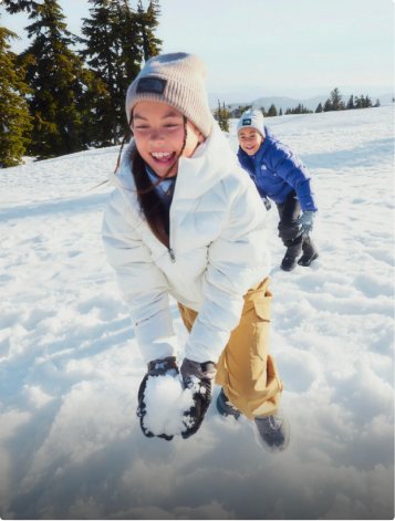 A picture of two kids playing outside in the snow wearing snow gear
