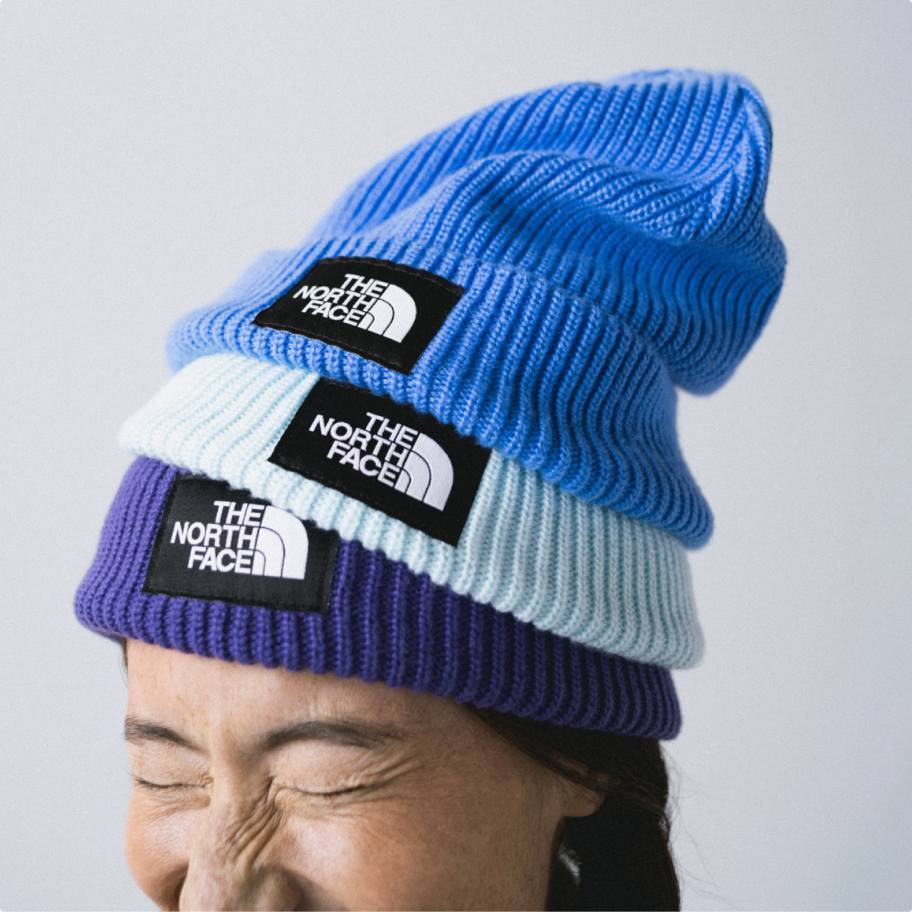 Woman squinting and wearing three beanies (sky blue, light blue and purple) stacked on top of each other.