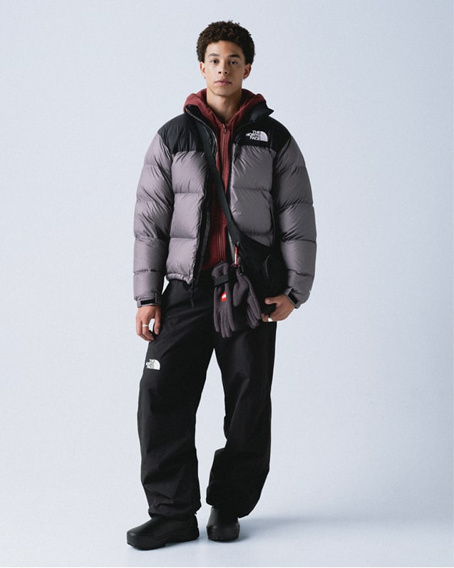 Man wearing maroon hooded zip-up with hood down, with gun-metal gray/black retro Nuptse jacket unzipped, a black crossbody bag and mountain gloves hanging from his waist.